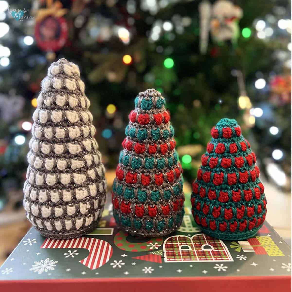 Three handmade crochet Christmas trees in different sizes and festive colors
