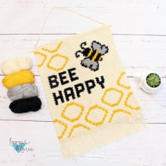 crochet wall hanging with a bee and bee happy printed on it