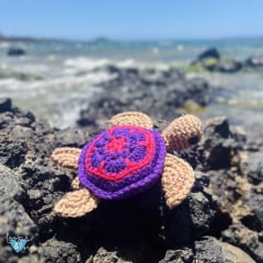 crochet mini sea turtle amigurumi on a rock by the ocean