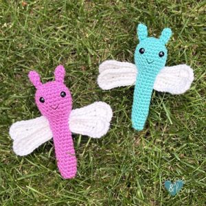 Brightly colored crochet dragonfly amigurumi with white wings, placed on grass