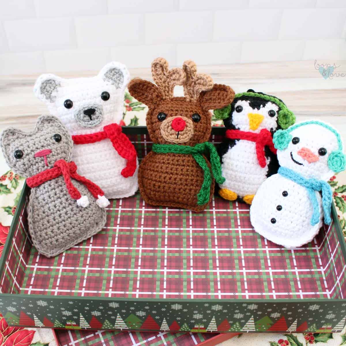 Five handmade crochet ragdoll Christmas ornaments featuring a reindeer, polar bear, penguin, snowman, and cat
